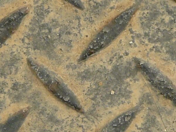 Metal tread texture in dark brown tones with leaf-like pattern on worn surface.